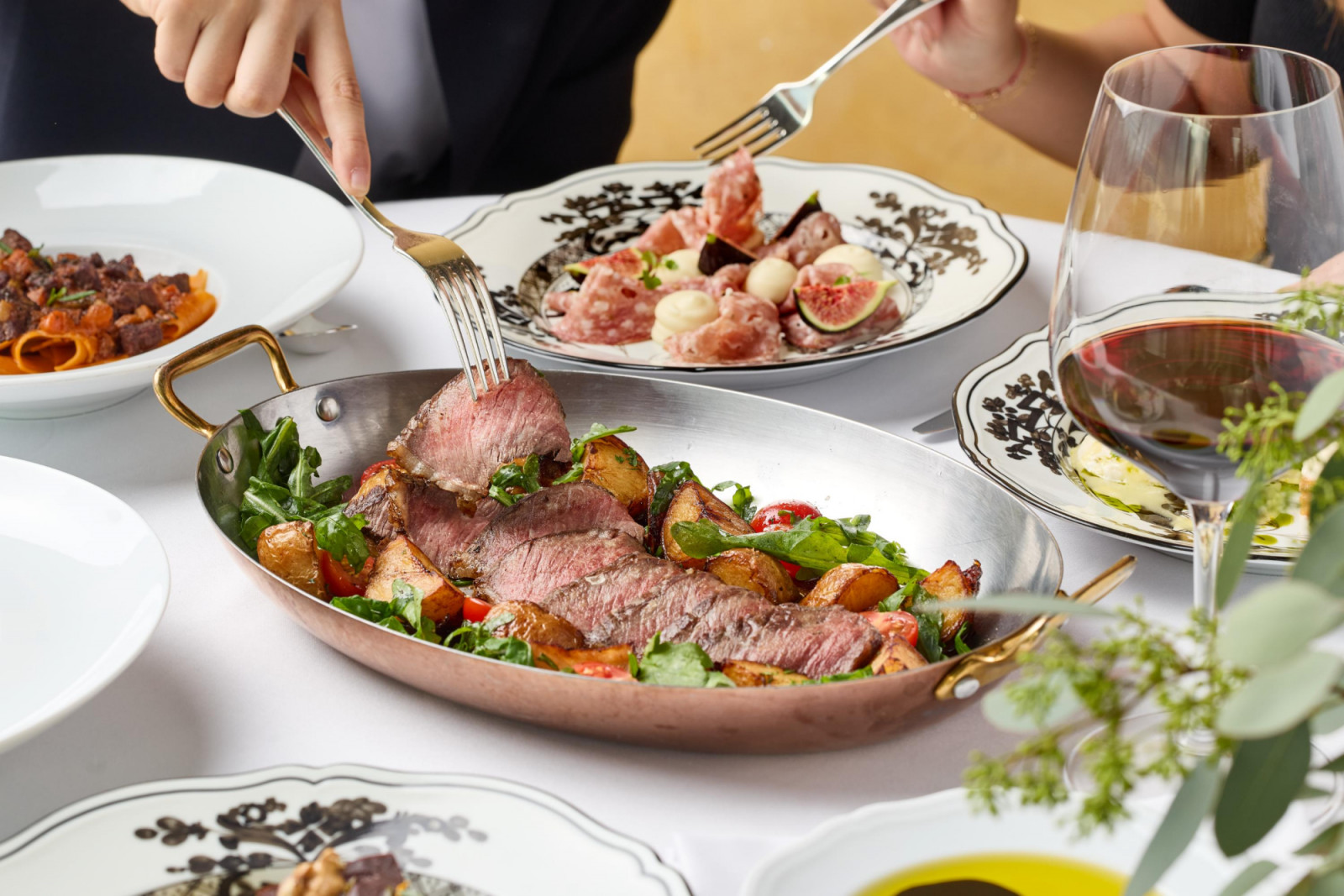 Guests savor a gourmet meal featuring sliced steak, charcuterie, and red wine.