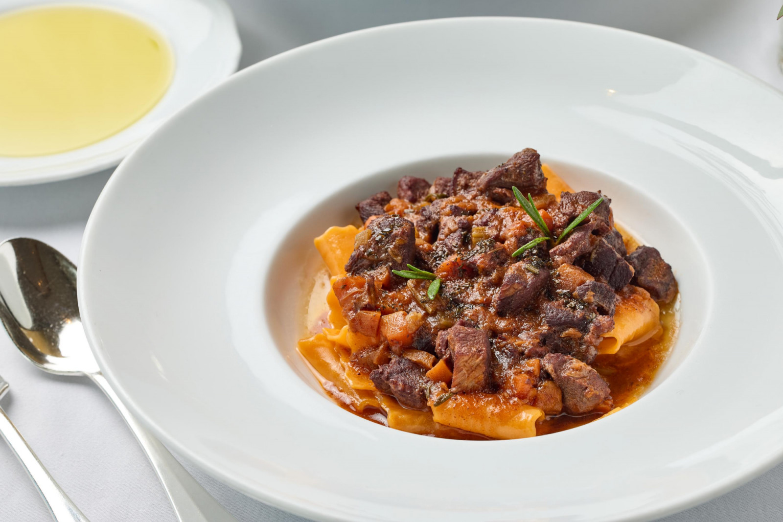 A classic Italian dish of paccheri pasta with rich, slow-cooked beef ragu, garnished with rosemary.