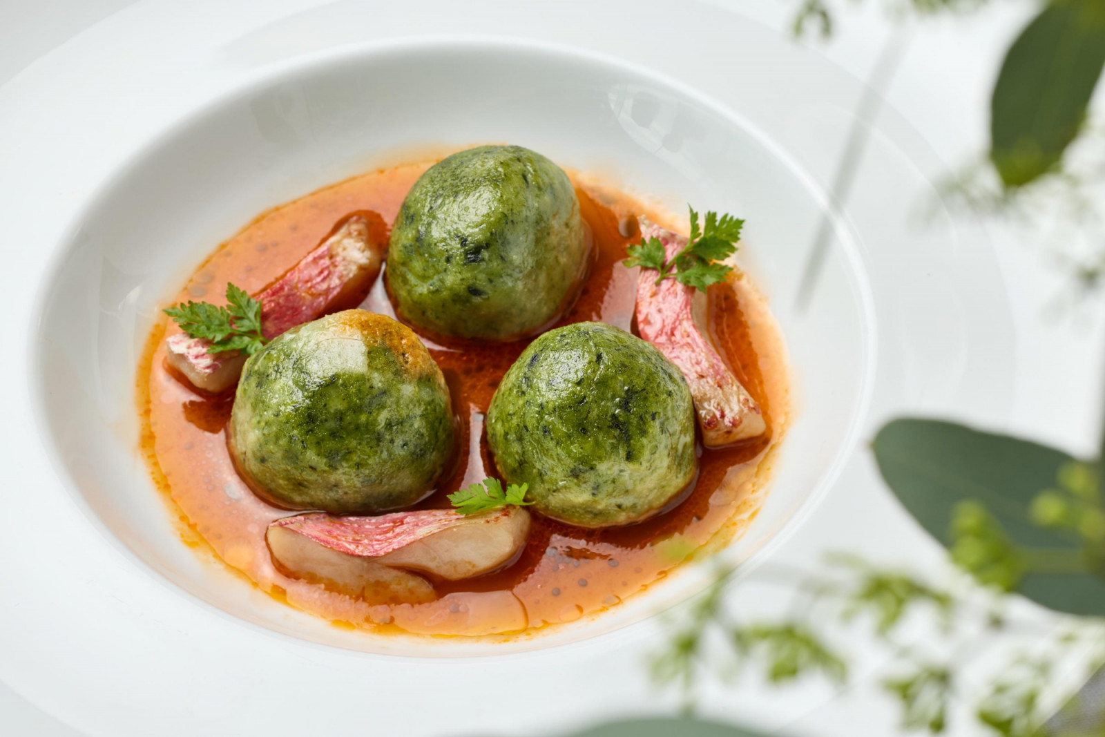 Spinach gnudi with pan-seared red mullet, served in a rich tomato and seafood broth, embodying Italian elegance.