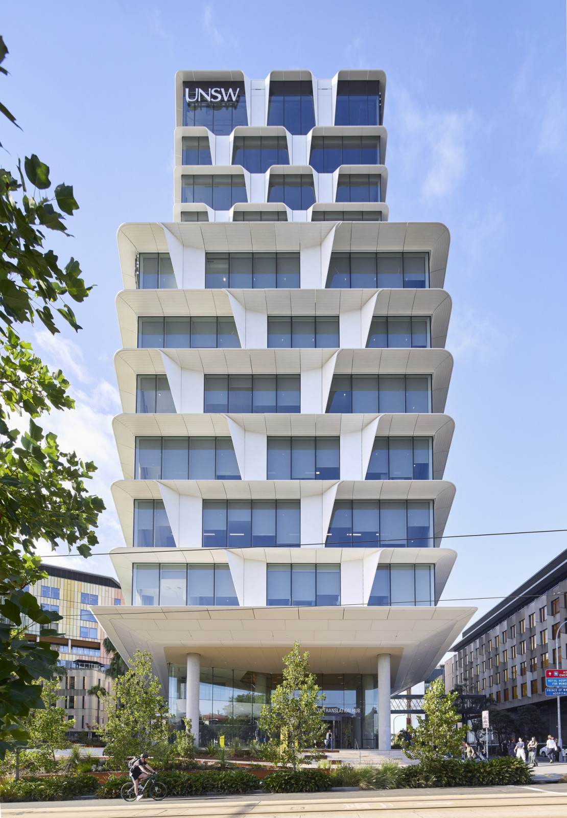 The façade’s angled white fins repeat down the building’s height, narrowing toward a boxier upper storey clad in darker glass (Photo: Hufton + Crow)