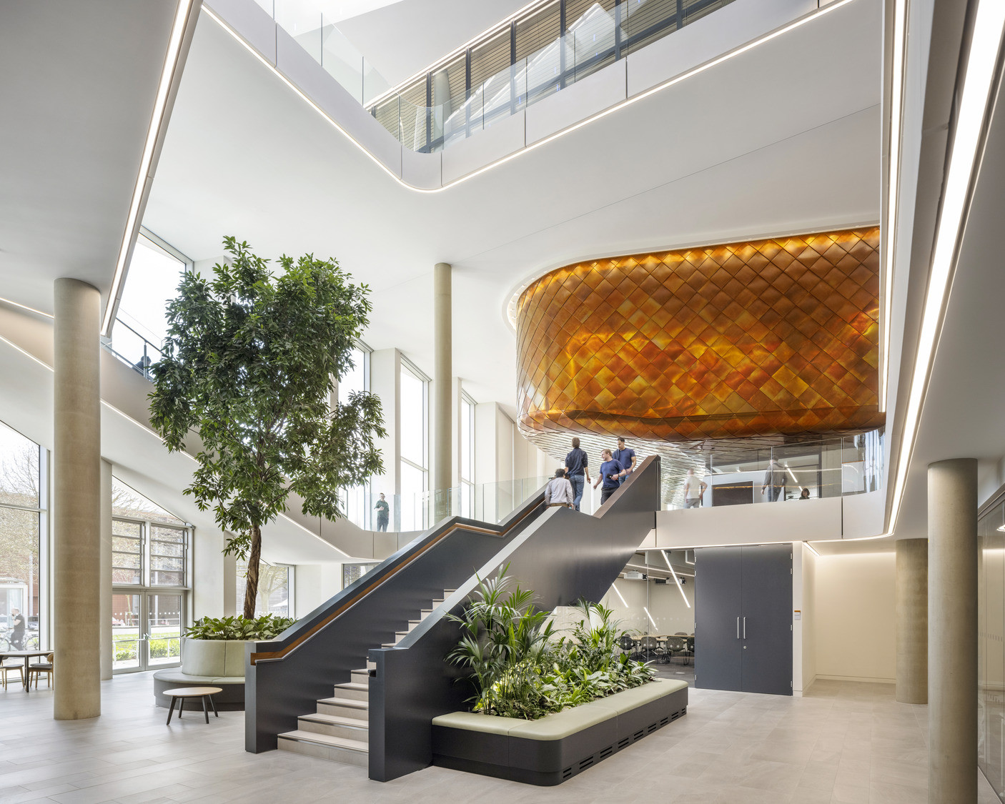 A dark steel staircase leads up towards the building’s signature copper-clad volume, suspended above the atrium on a faceted underside (Photo: Kilian O’Sullivan)