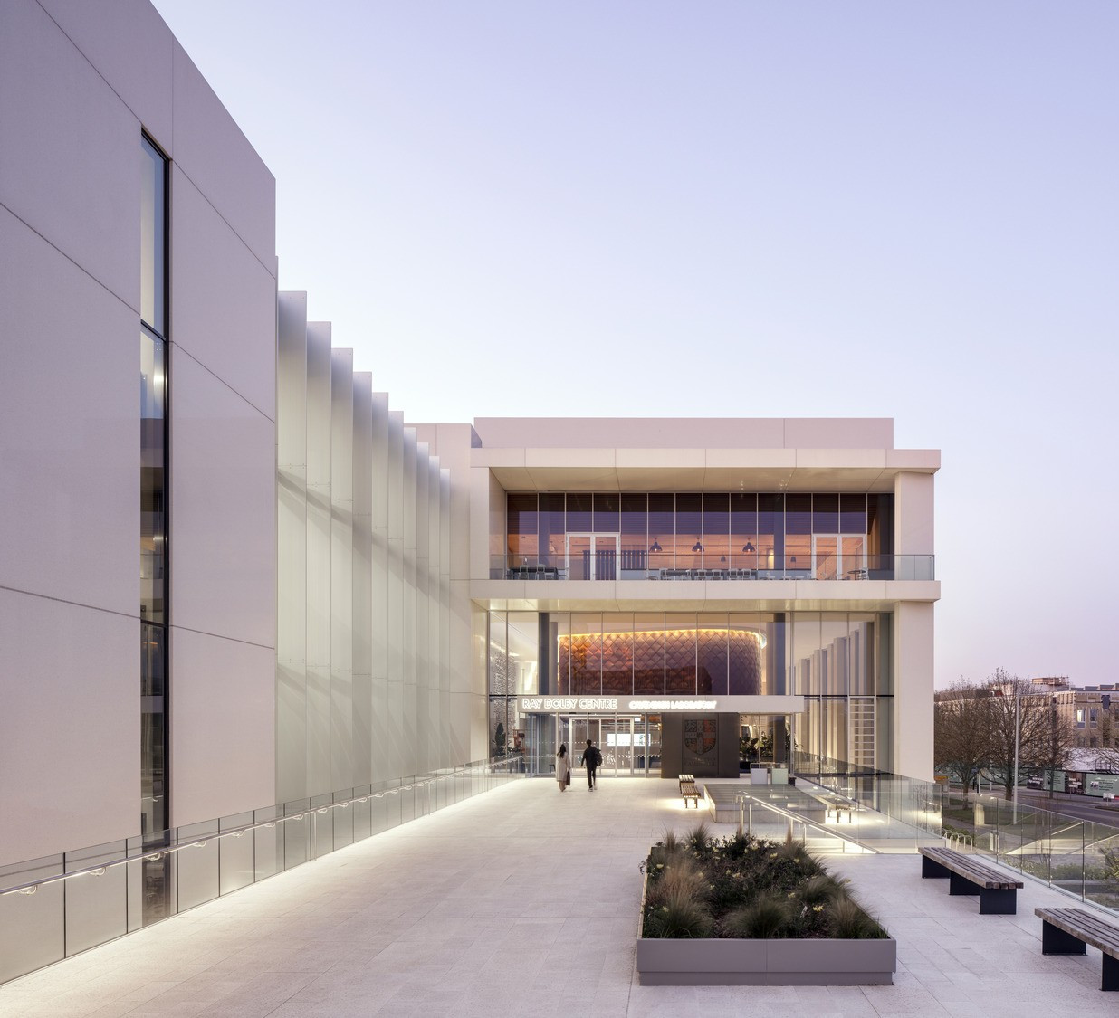 At dusk, the entrance to the Ray Dolby Centre glows beneath a copper-clad lecture theatre suspended above the ground floor (Photo: Kilian O’Sullivan)