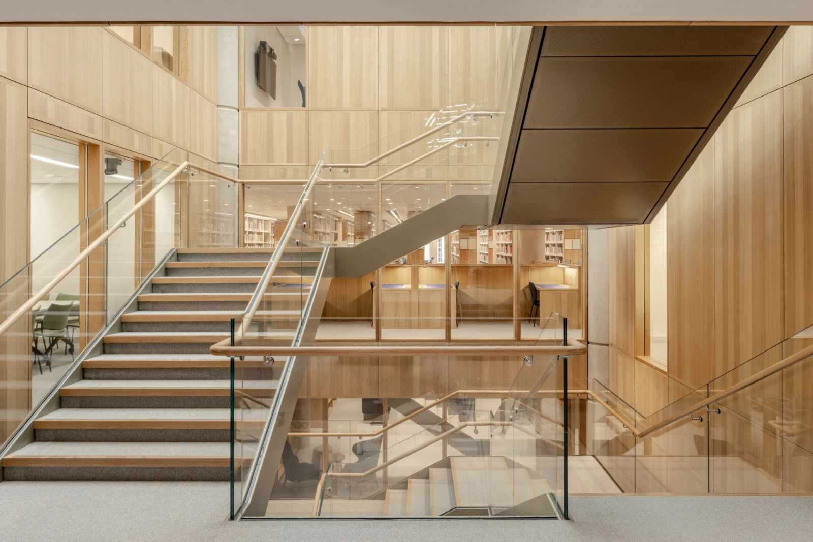 A timber-clad staircase descends past library shelving visible through glass balustrades (Photo: Hufton + Crow)