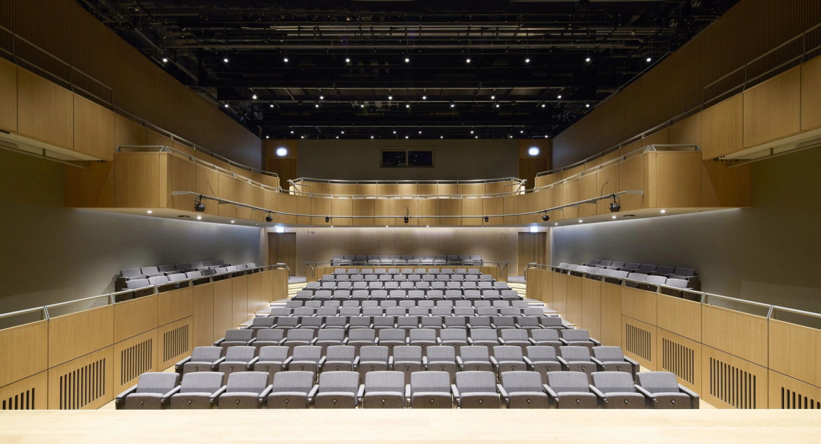 Rows of grey upholstered seating fill the 500-seat concert hall beneath a blacked-out technical ceiling (Photo: Hufton + Crow)