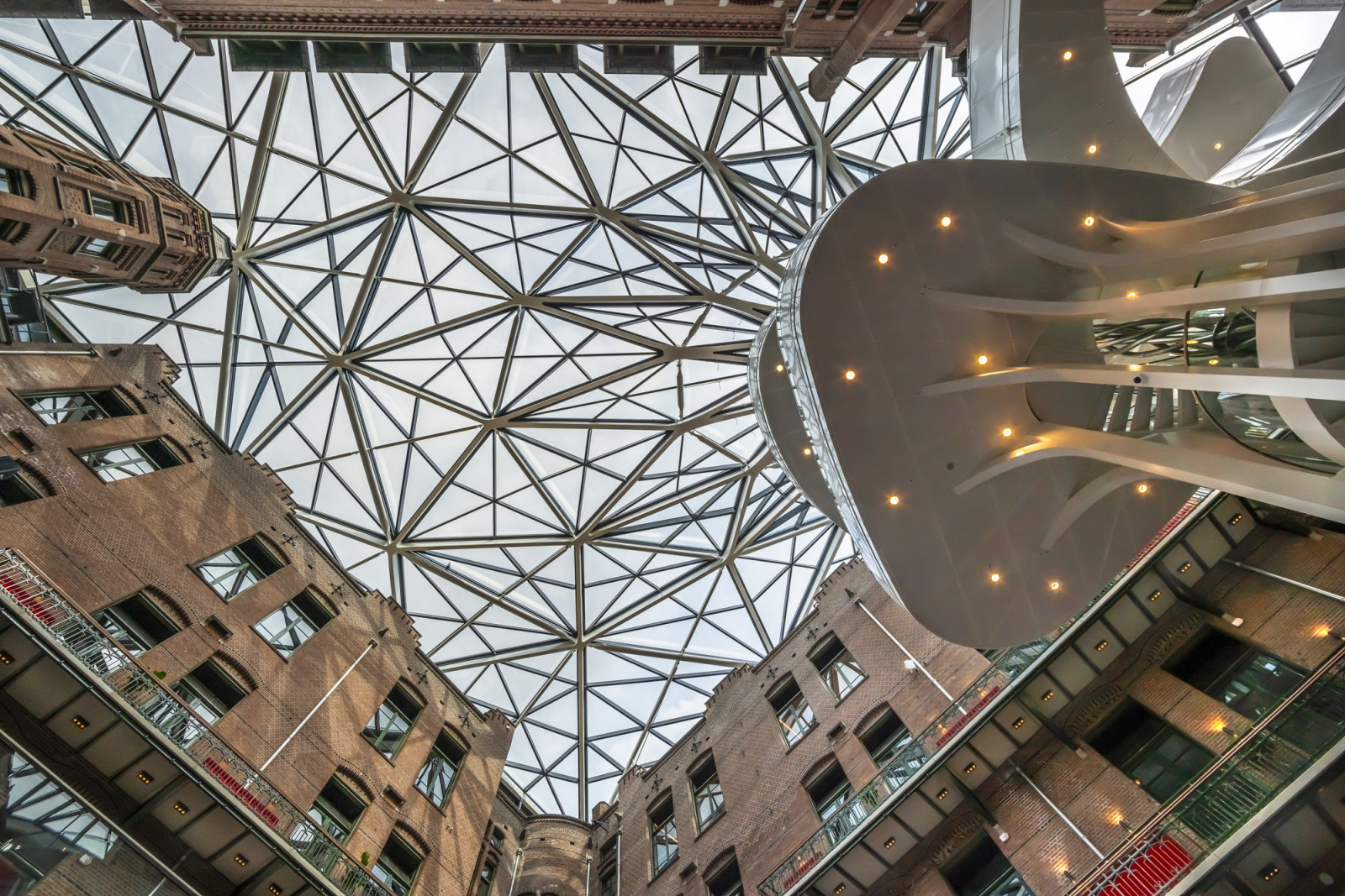 A triangulated steel grid spans the atrium roof, framing the historic complex’s brick façades on either side (Photo: Jannes Linders)