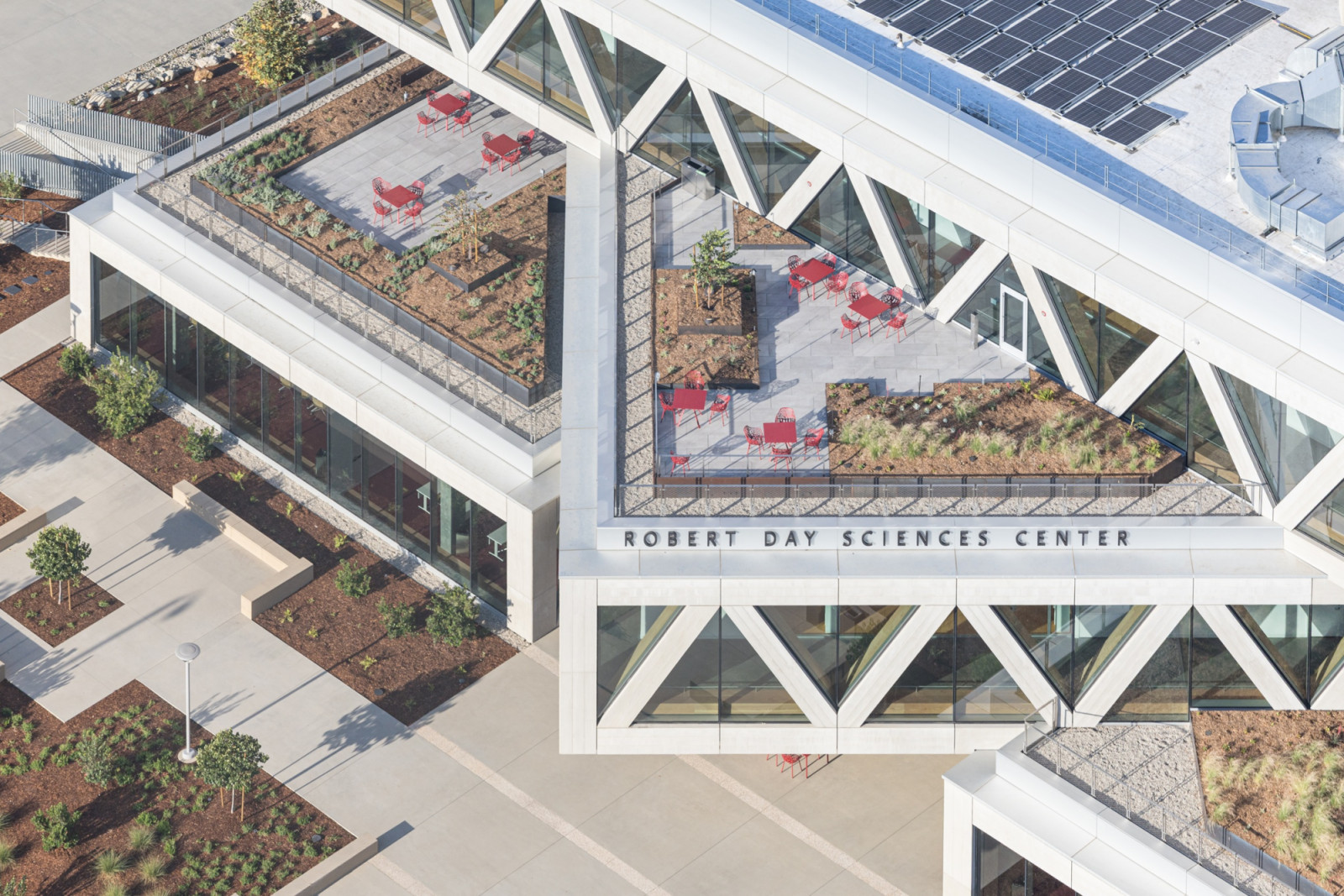 Red furniture sets punctuate a rooftop terrace planted with drought-tolerant landscaping, set beneath the building’s triangulated concrete façade (Photo: Laurian Ghinitoiu)