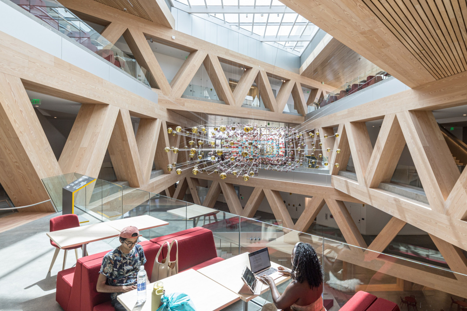 Timber trusses cross the atrium in a repeating triangular pattern, with a suspended sculptural installation of coloured spheres hanging at its centre (Photo: Laurian Ghinitoiu)