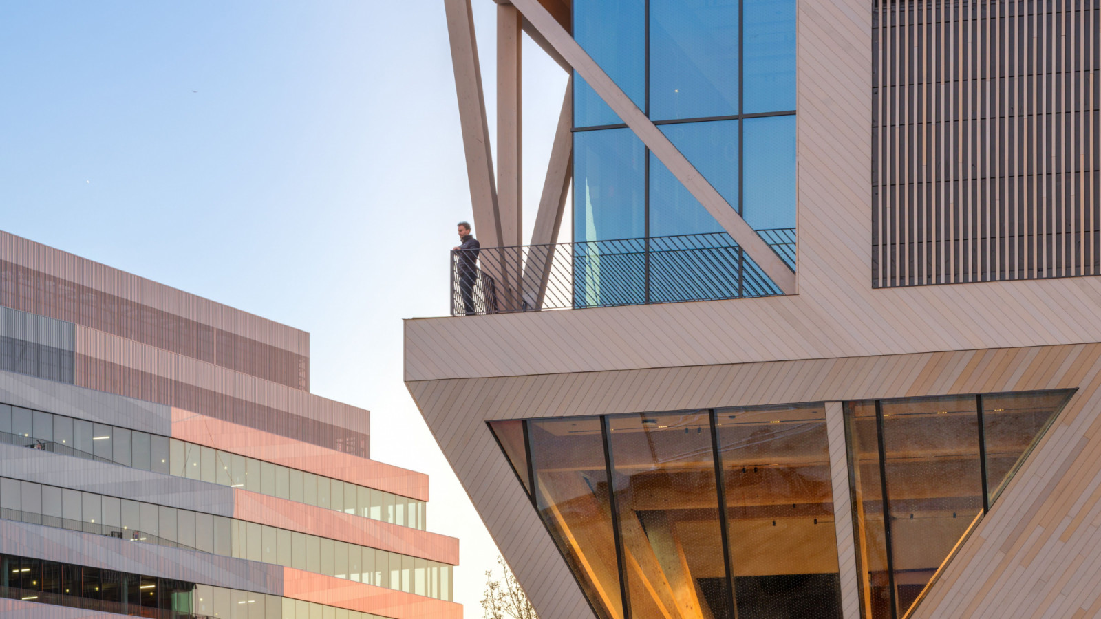 A visitor looks out from a timber-framed terrace, with diagonal cross-bracing supporting the cantilevered volume above (Photo: Jason O’Rear)