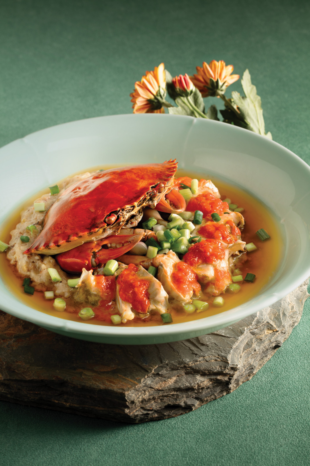 A refined crab dish featuring steamed crab on a delicate base, topped with vibrant red sauce and fresh scallions.