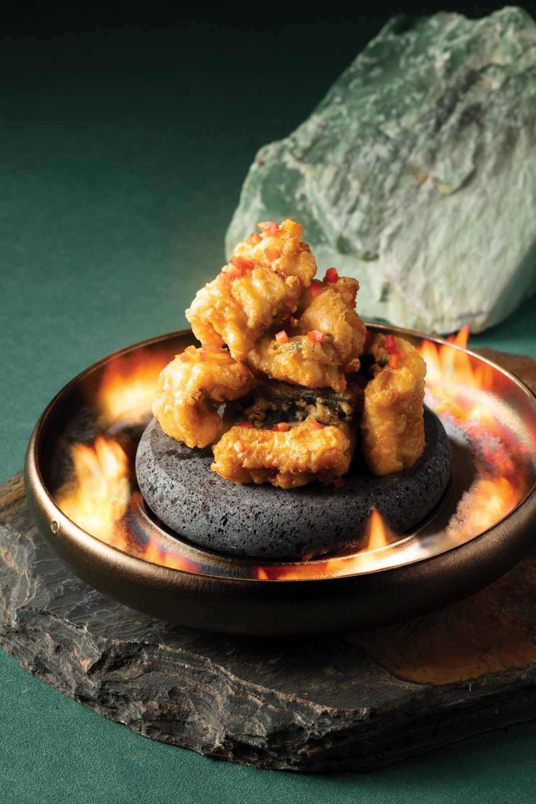 Crispy fried bites with diced red chili, presented sizzling on a hot volcanic stone.