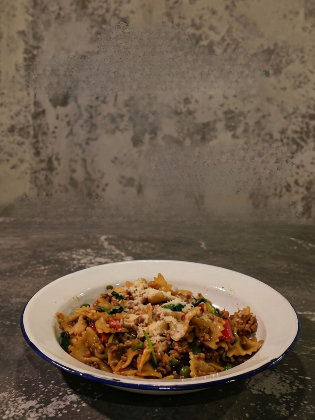 Farfalle pasta with a savory meat ragu, fresh peas, and bell peppers, topped with grated cheese.
