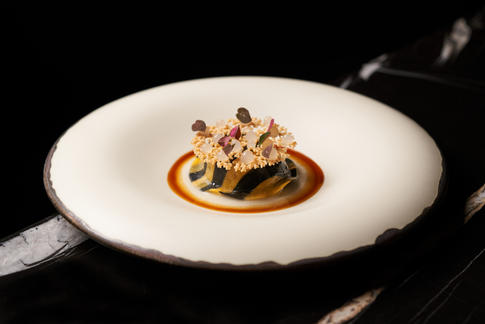 A plated culinary dish features striped layers of pasta or vegetable, delicate coral tuiles, micro-herbs, and a rich sauce.