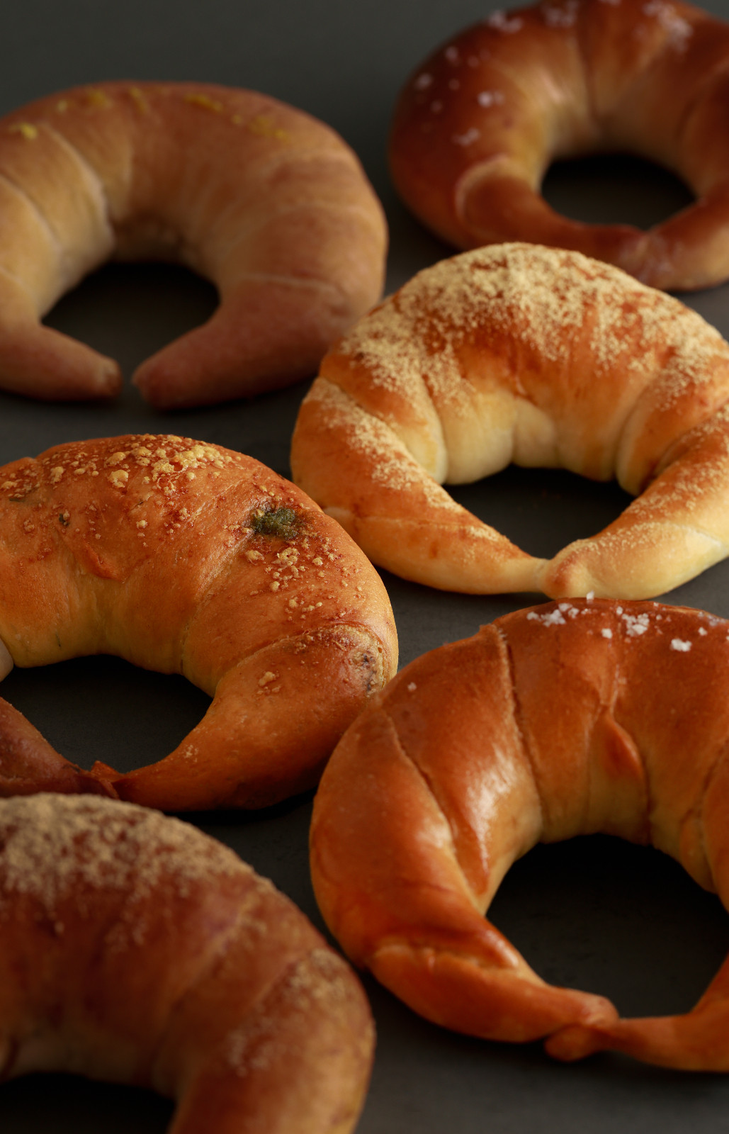 An assortment of golden crescent rolls, some topped with sugar, salt, or savory herbs.