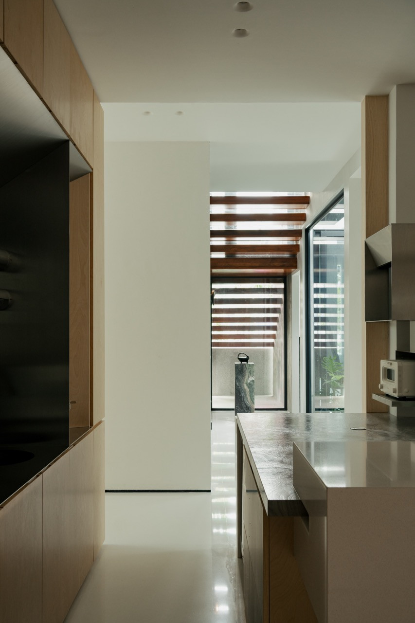 A corridor in polished stone and plywood, leading toward a slatted timber canopy and a marble plinth beyond
