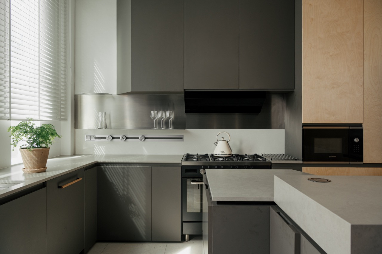 A kitchen in matte grey cabinetry with a stainless steel splashback, gas hob and a birch plywood pantry wall