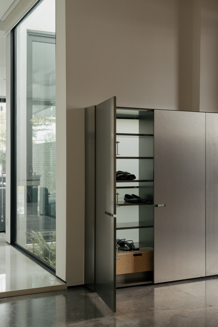 A tall storage cabinet with a mirrored door, revealing shelved footwear beside a floor-to-ceiling window