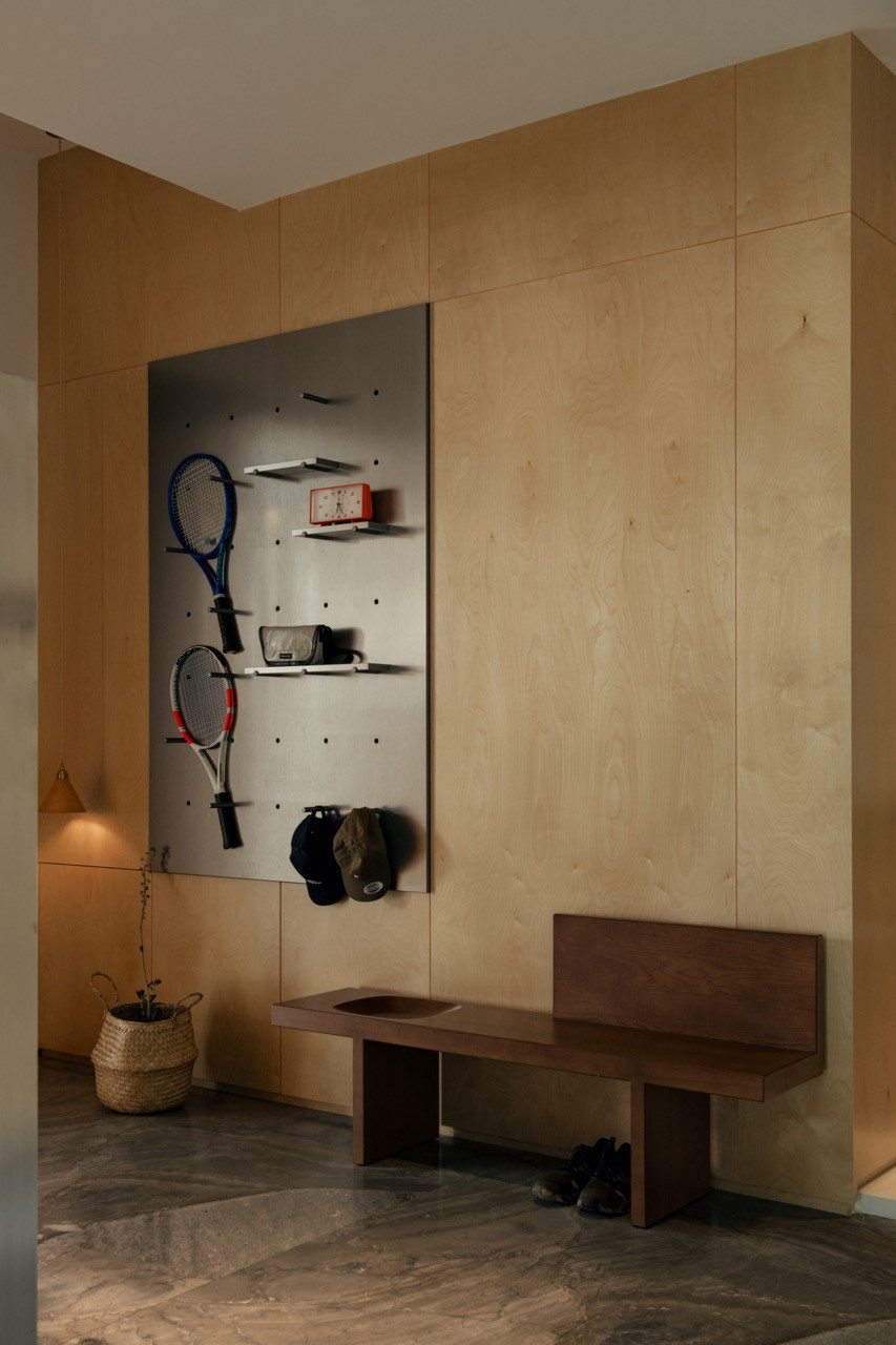 A mudroom wall fitted with a perforated steel panel for storing tennis racquets, caps and bags, above a timber bench