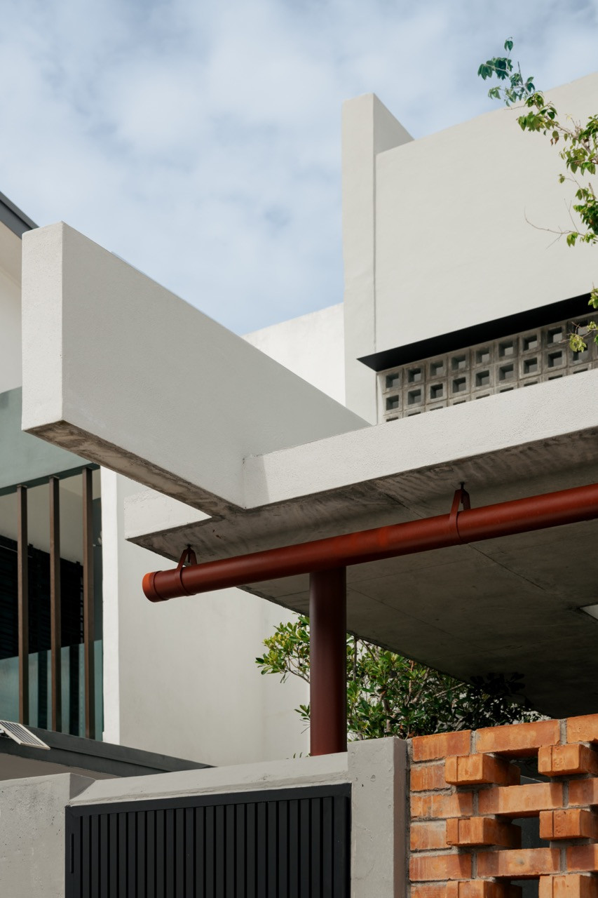 A detail of the house’s cantilevered concrete eaves, with a rust-red downpipe against a brick lattice wall