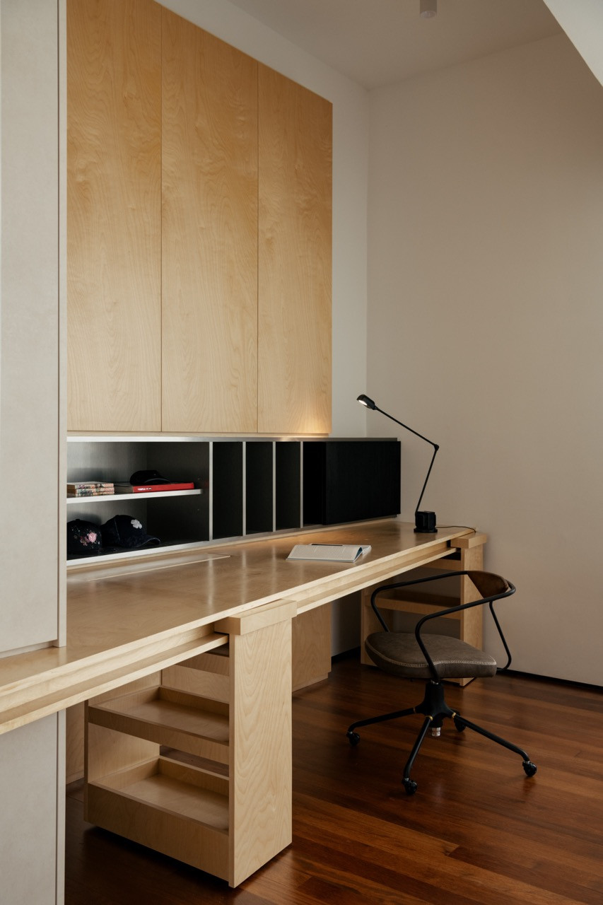 A built-in home office nook in birch plywood, with a slim desk lamp and a leather task chair