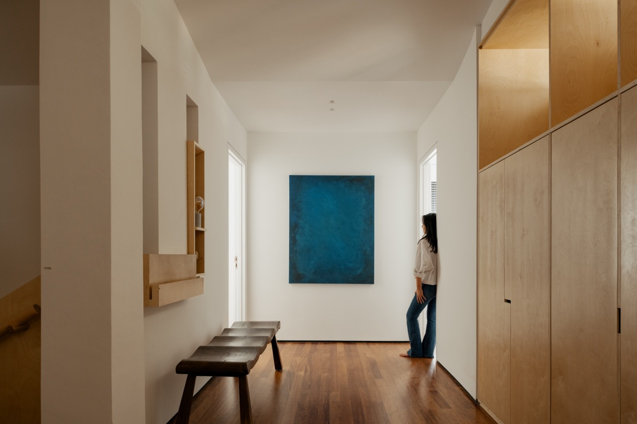 A hallway in white plaster and timber flooring, with a blue abstract painting and a low wooden bench