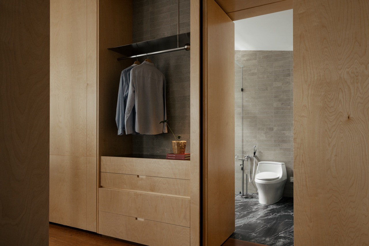 A wardrobe interior in birch plywood, opening directly onto an ensuite finished in black marble