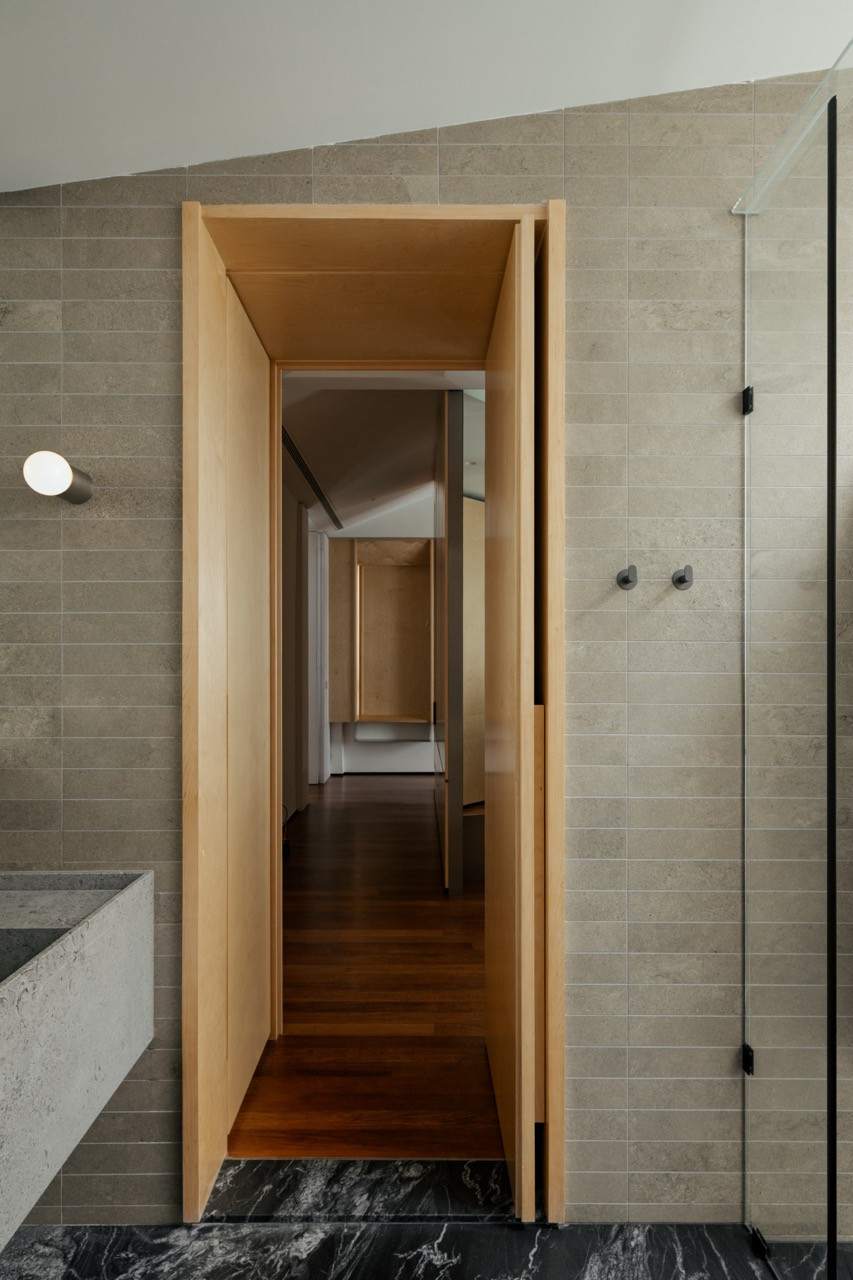 A plywood-framed doorway opening from the black marble bathroom onto a timber-floored corridor