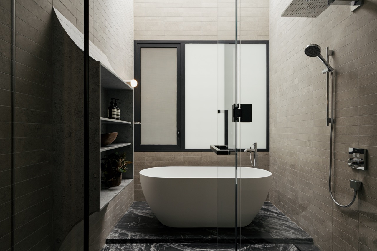 An ensuite bathroom with a freestanding tub set on black marble flooring, beneath a rain shower fitting