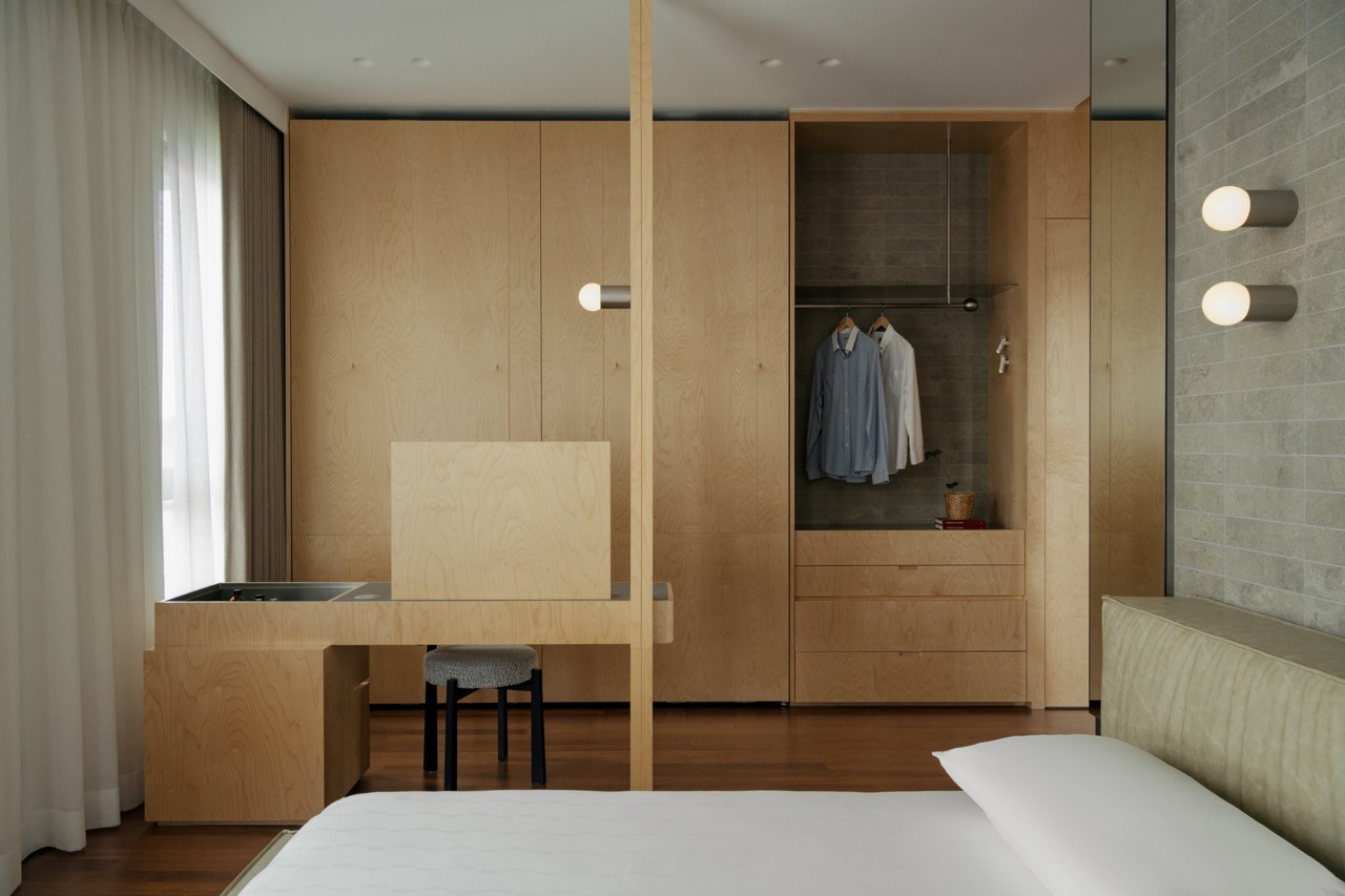 A bedroom dressing area combining plywood joinery, an open wardrobe niche and a stone-tiled backdrop