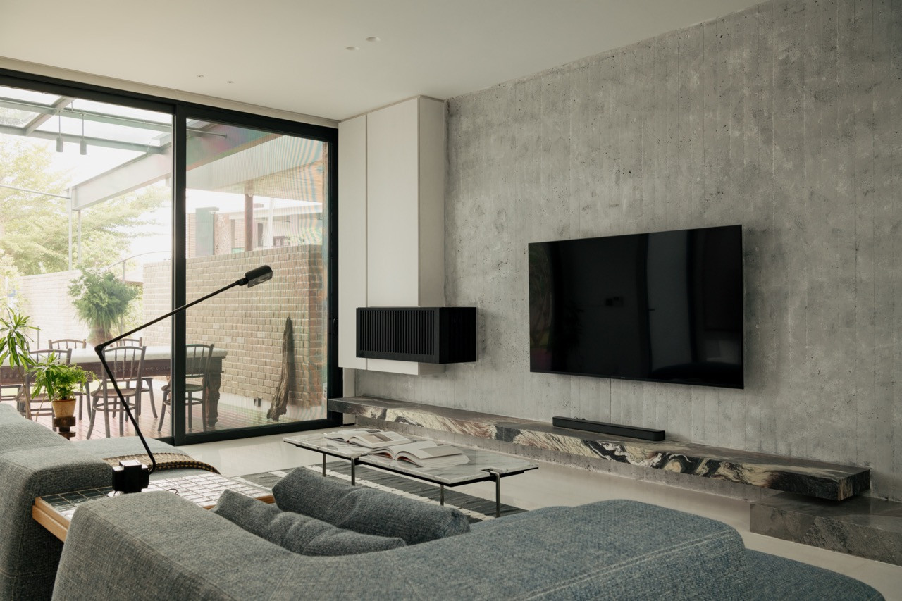 A television wall in off-form concrete, with a slab marble console beneath and glimpses of the deck outside