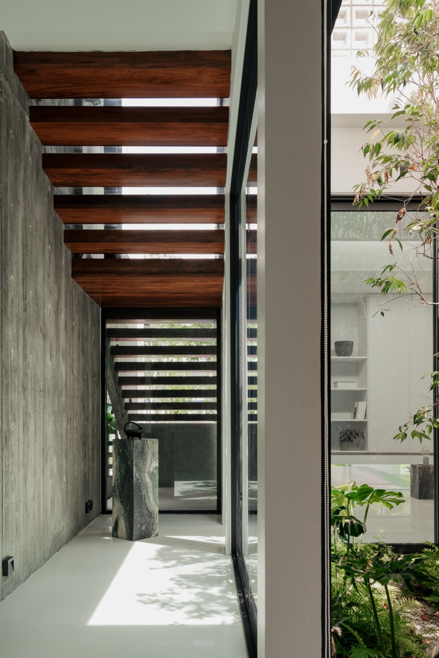 A covered walkway with a timber-slatted ceiling and off-form concrete wall, overlooking a planted courtyard