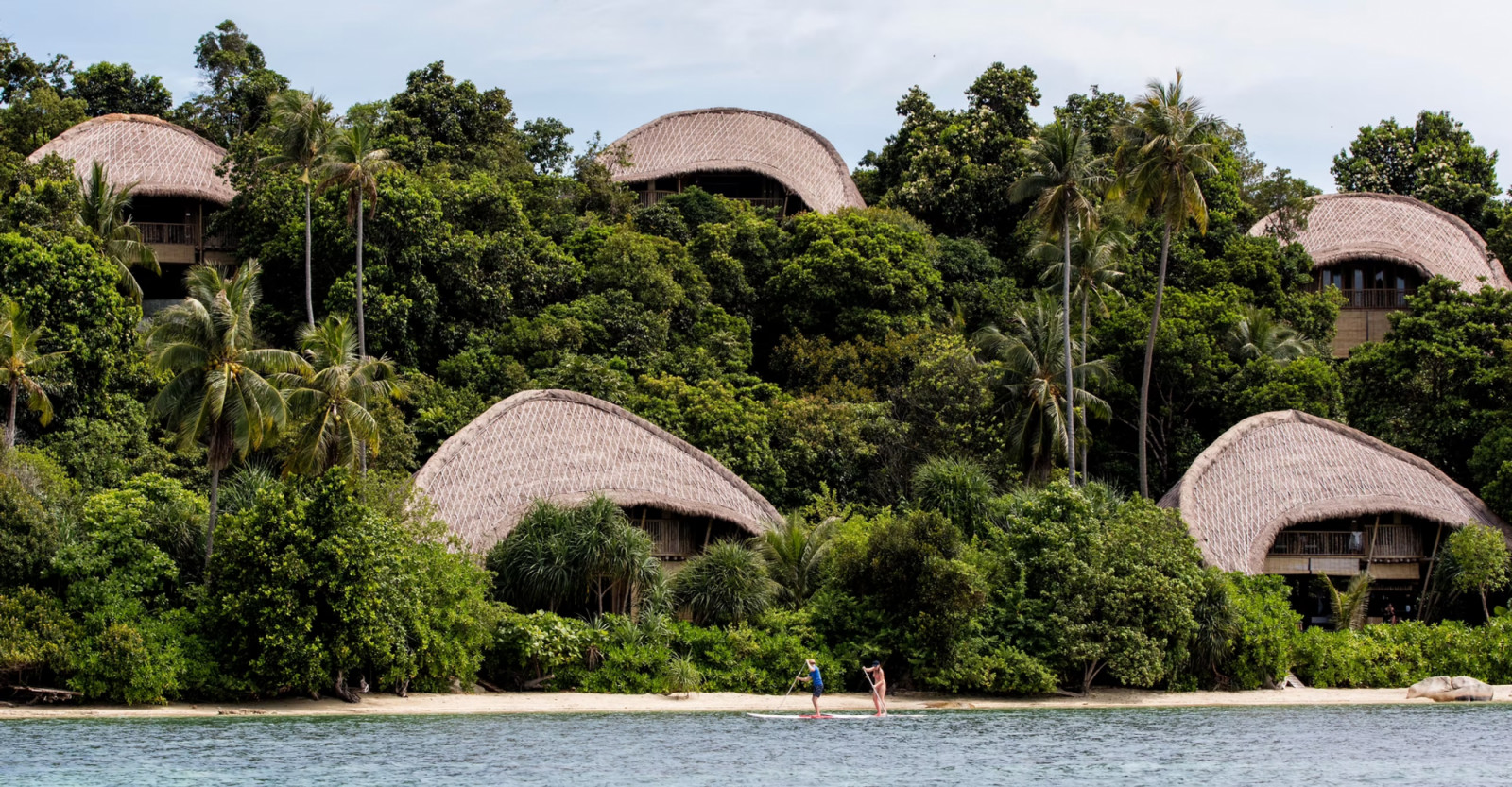 Cempedak Island’s cluster of bamboo villas seen from the water, their curved roofs rising above the mangrove canopy along the shoreline