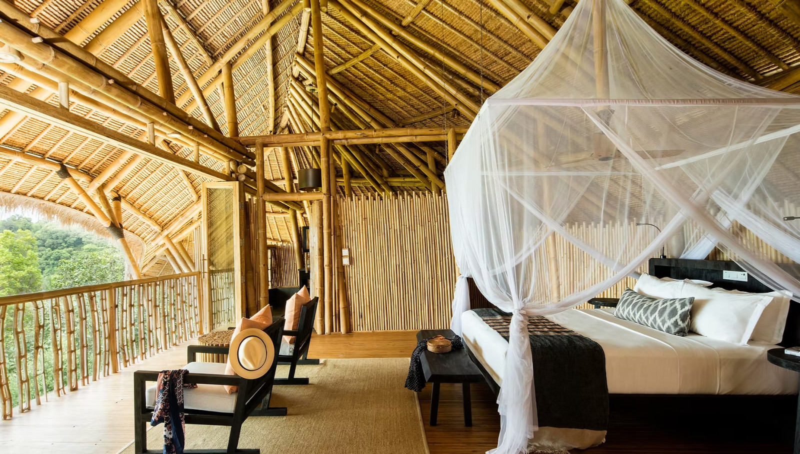 Inside a Cempedak Island villa, exposed bamboo trusses and a woven ceiling frame a mosquito-netted bed and open-air balcony over the treetops
