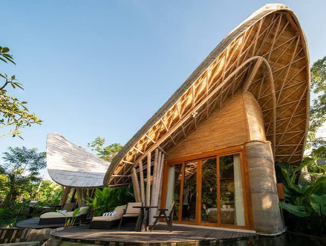 A guest villa at Ulaman, its curved bamboo roof structure exposed in a woven lattice above rammed-earth walls and glazed doors