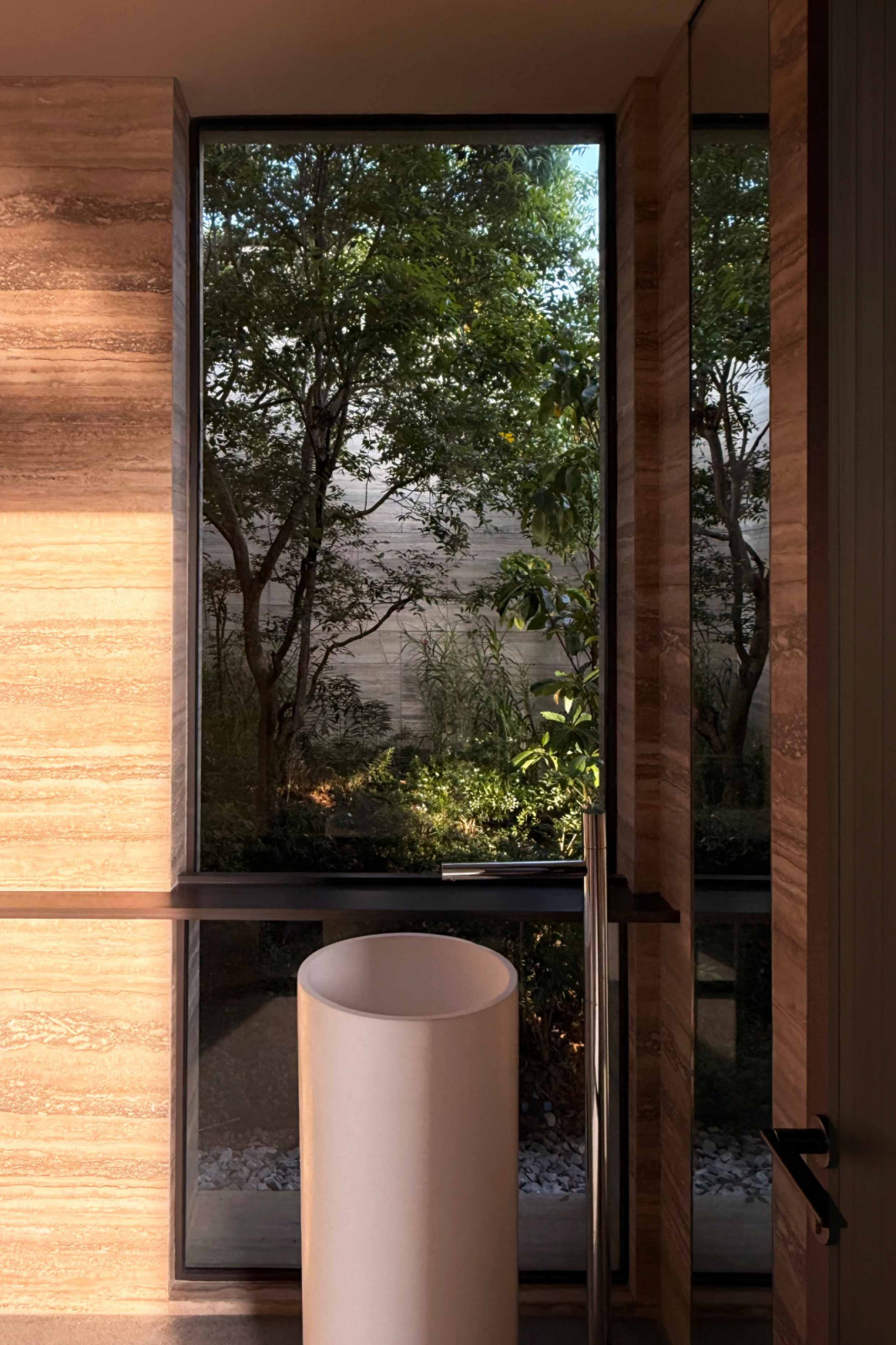 Even the bathroom is drawn into the house's layered sightlines, its travertine walls framing a private pocket of greenery