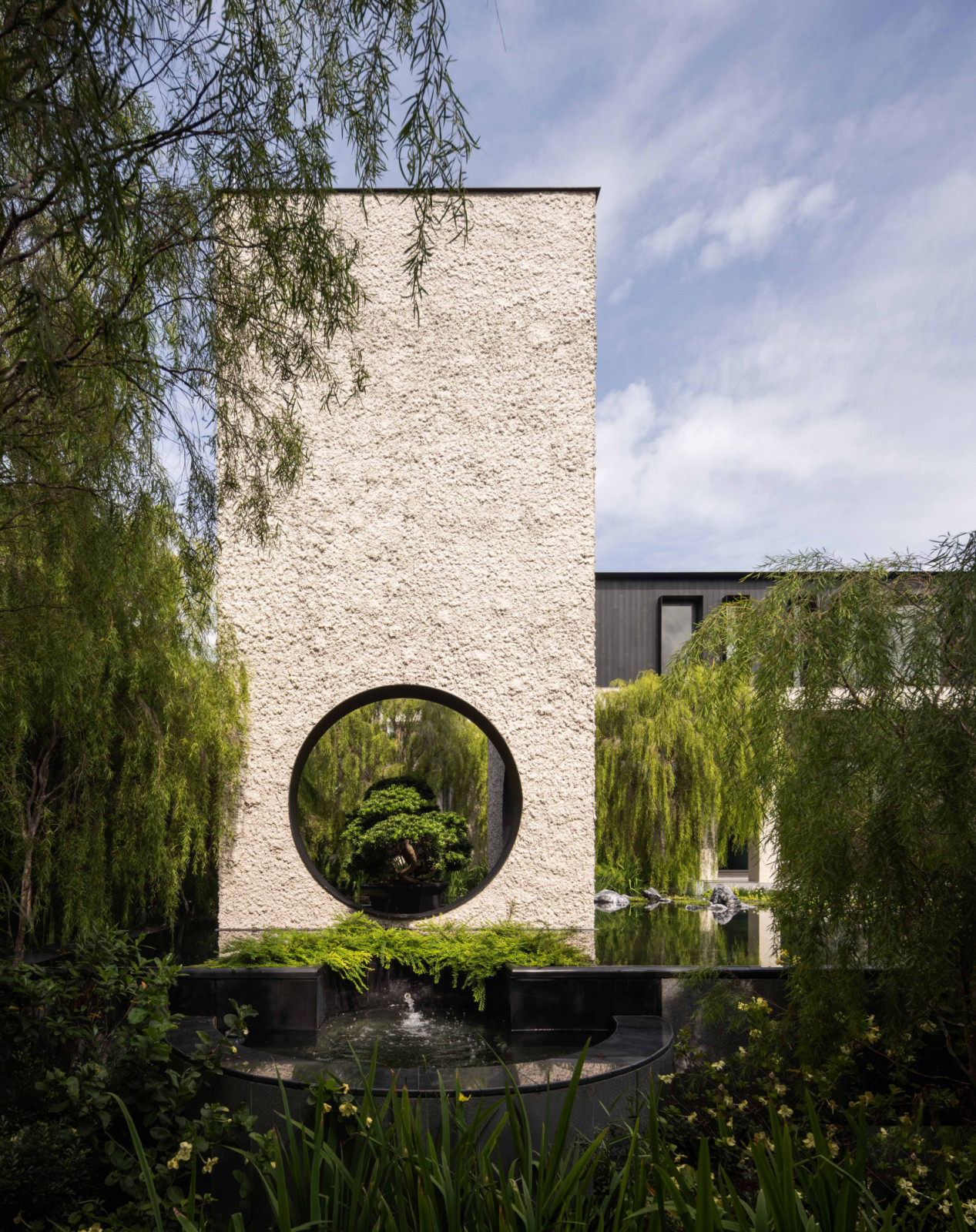 The moon pavilion’s circular portal reflects in the surrounding pool, its fallen-moon abstraction framed by the drooping foliage of the silver weeping tea tree