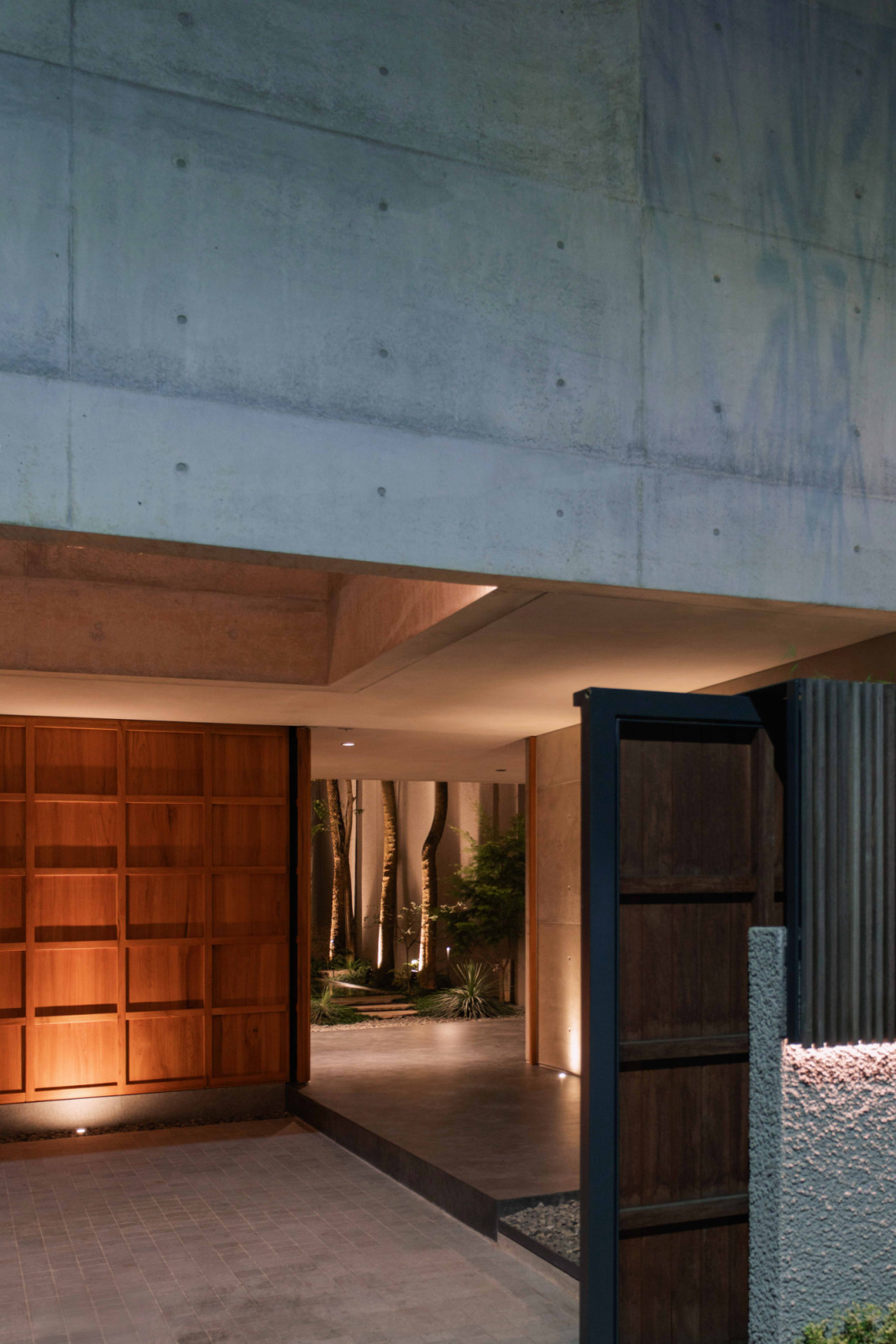 At night, the timber entrance door frames a lit garden path leading into Lift House