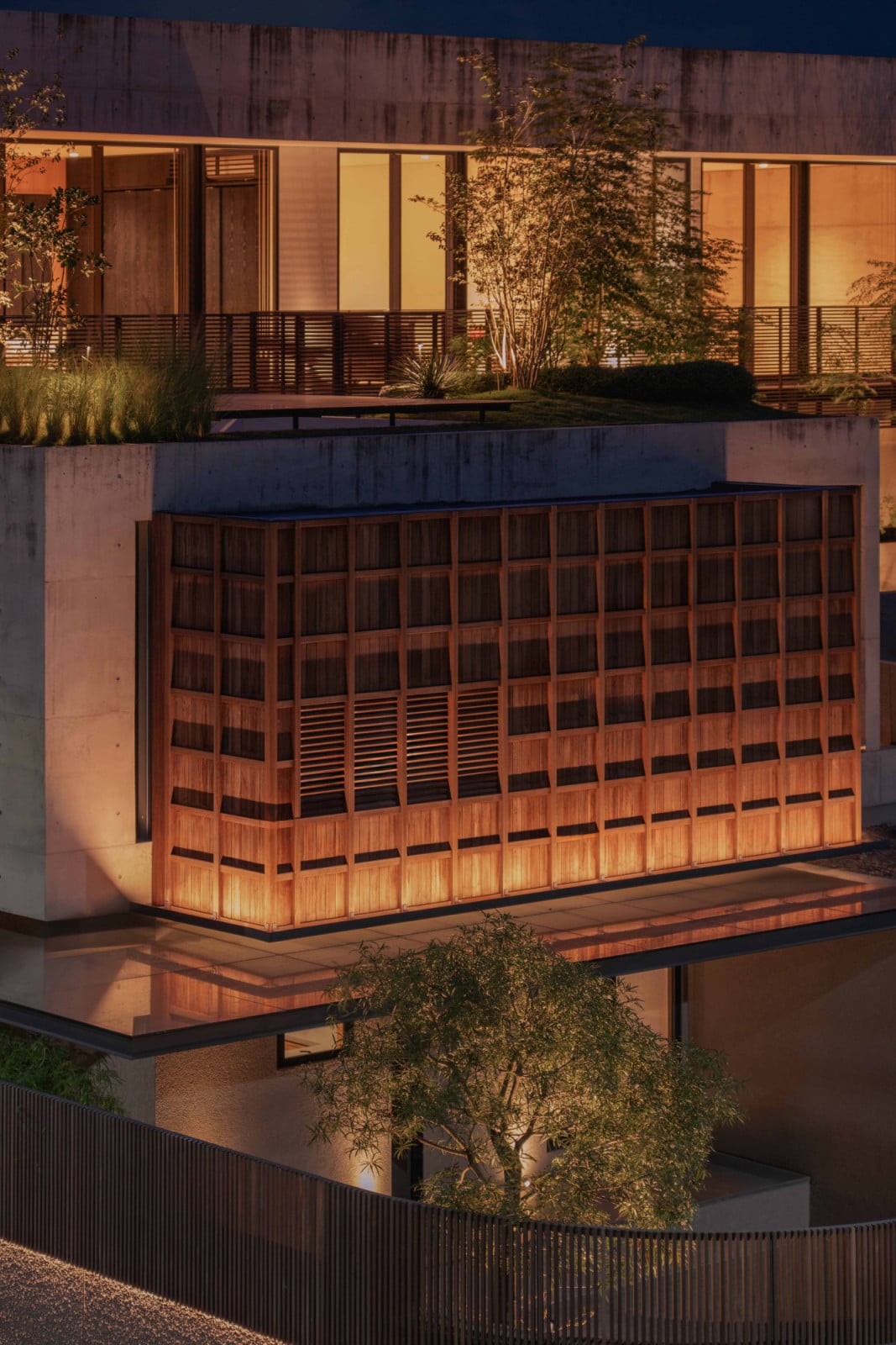 At night, Lift House's timber-screened volume glows against its board-marked concrete shell in Bandung