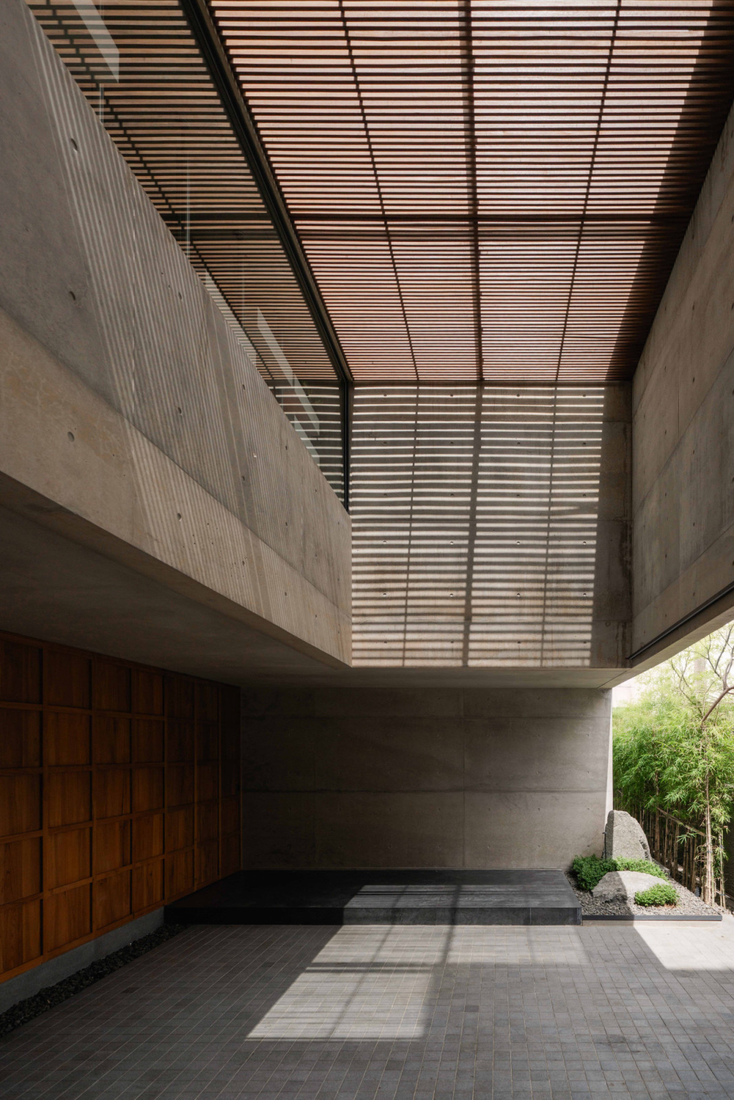 Timber slats overhead cast striped shadows across the concrete carport