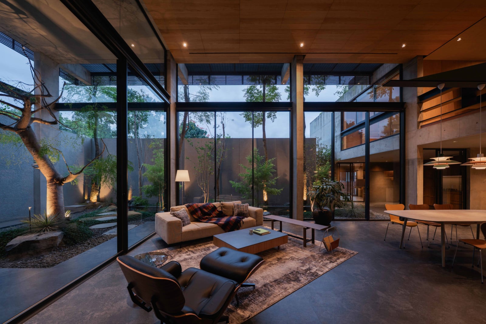 At dusk, Lift House's living and dining spaces glow between glass walls and garden trees