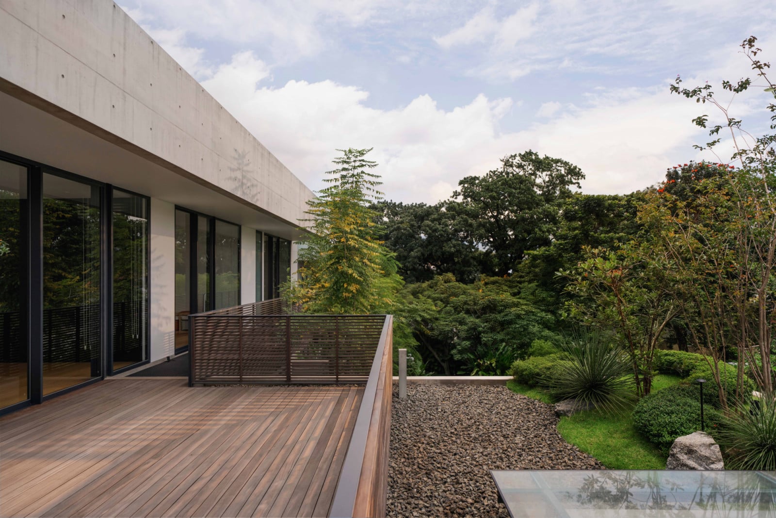 The upper-floor terrace’s greenery spills visually into the adjacent park beyond, blurring where the garden ends and the neighbourhood begins
