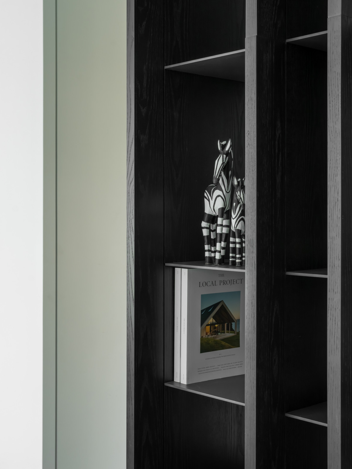 A built-in shelving unit in dark-stained wood displays books and decorative objects, dividing space without the need for a blank wall.