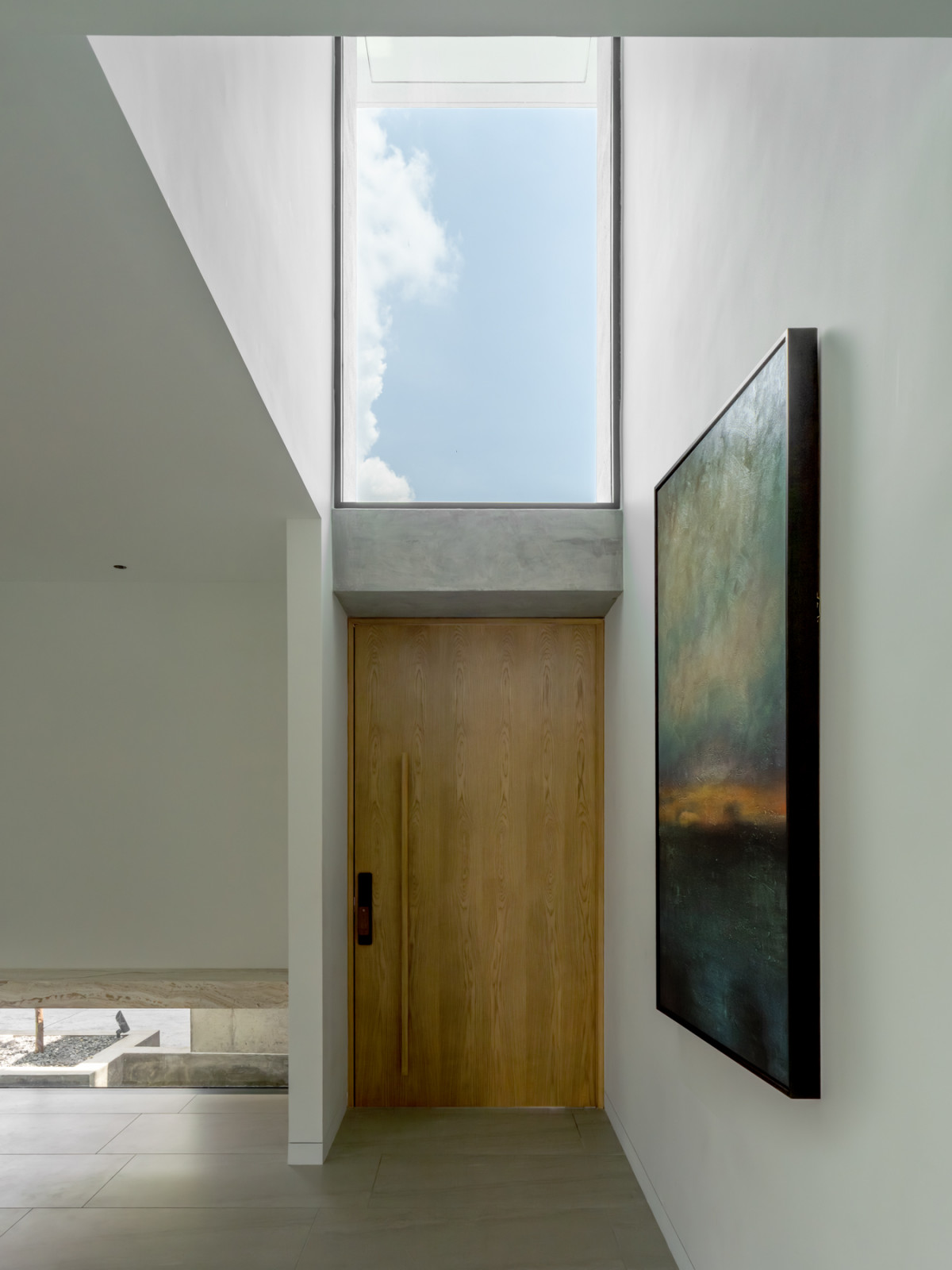 The timber front door sits beneath a tall skylight, with an artwork hung on the adjacent wall