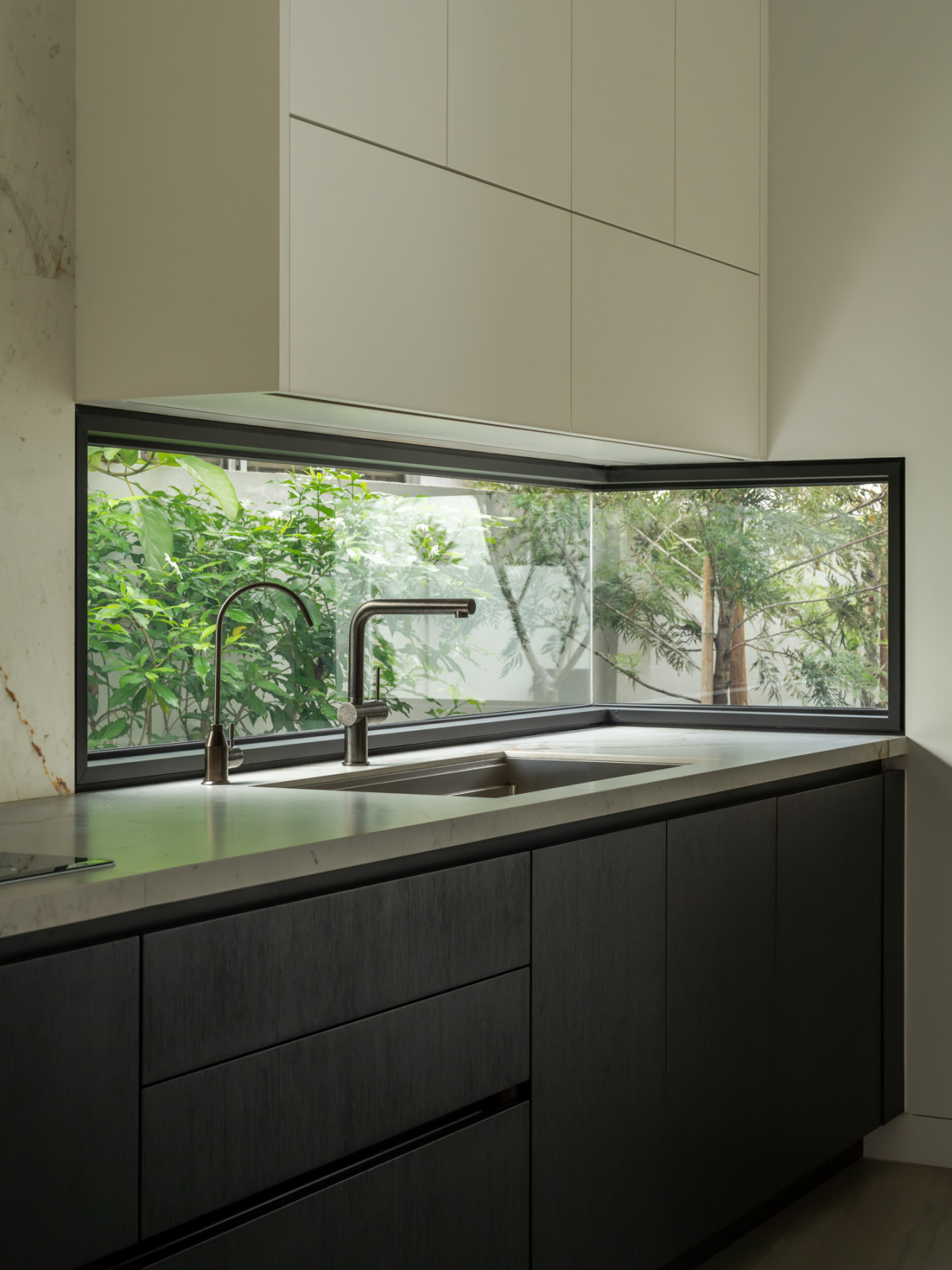 A corner window above the kitchen sink looks directly onto the garden’s greenery, with a Bulthaup cabinet in matte black below