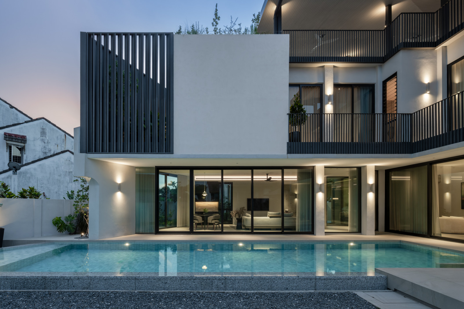 At dusk, the pool runs along the rear façade, with a steel-clad volume rising above the living areas
