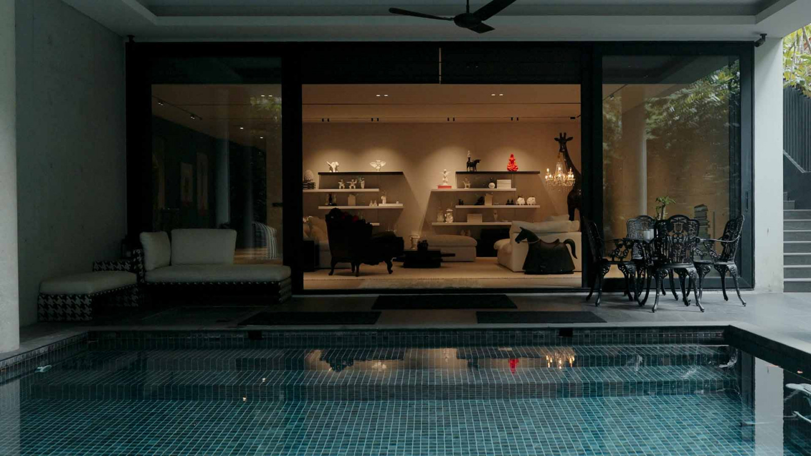 Sunset Vale’s pool and living room, seen together through glass at dusk