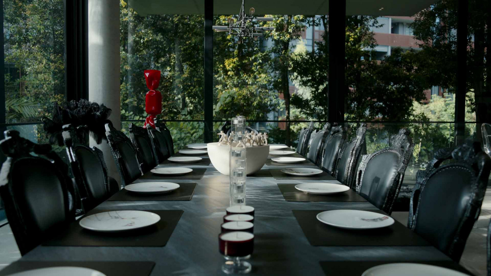 The dining table set for a gathering, sculptures perched on every chair back
