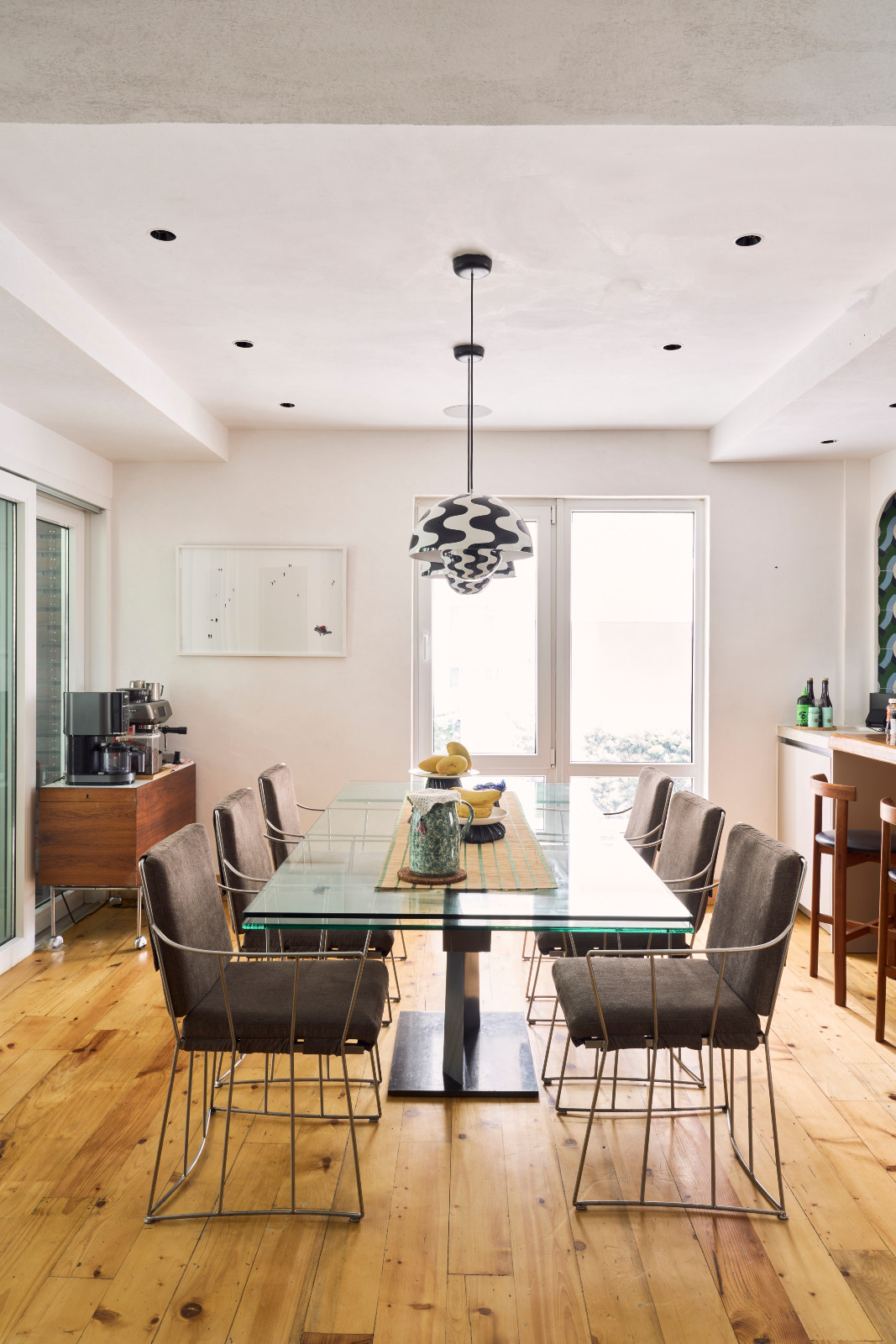 The extendable dining table in glass is topped with bold print pendant lamps