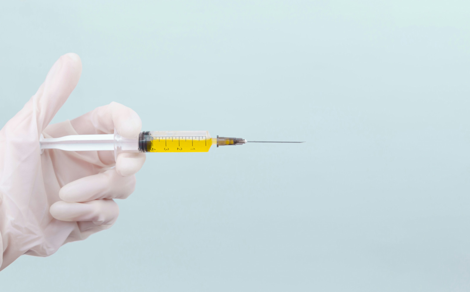 A gloved hand holds a syringe containing a yellow solution, often used in aesthetic treatments.