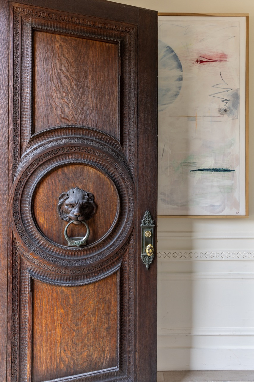 A carved oak door with a bronze lion's-head knocker opens onto the entry hall, where an abstract painting hangs