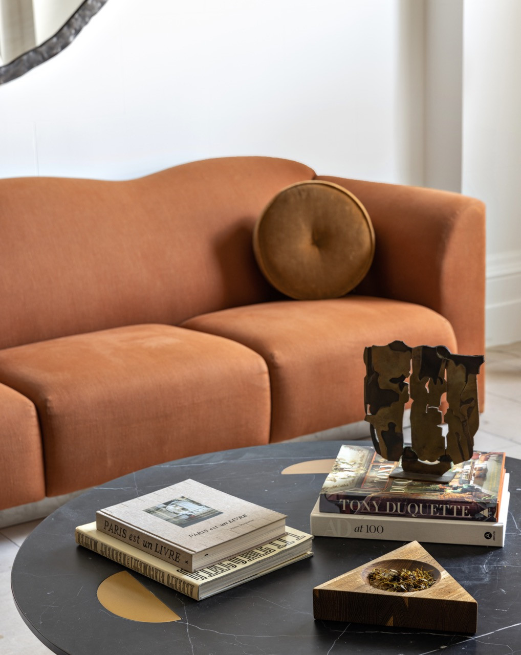 A stack of design books, including titles on Tony Duquette and Paris, sits on a black marble coffee table beside a bronze sculpture